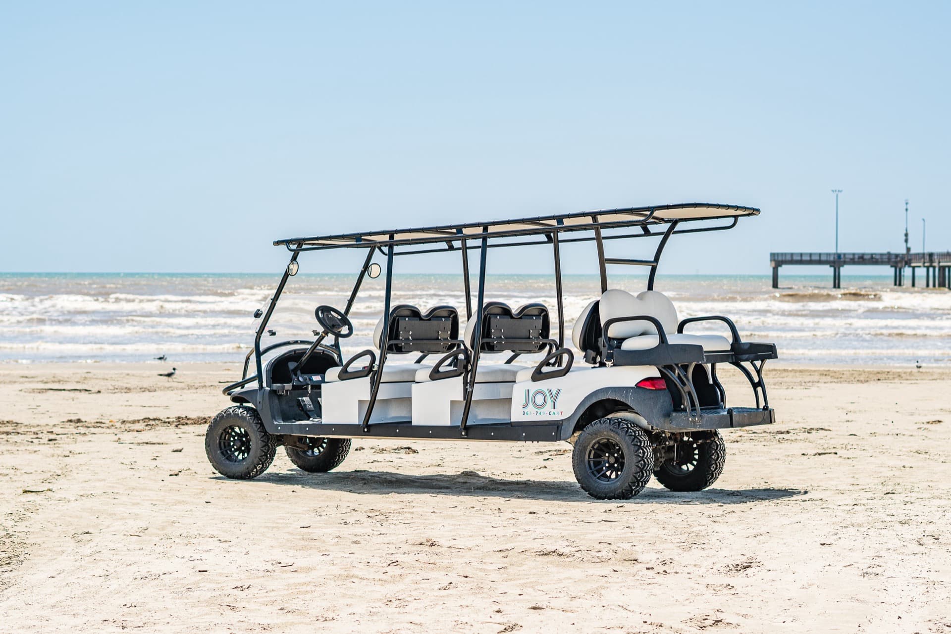 Joy eight-passenger golf cart parked on Port Aransas beach with Horace Caldwell Pier in the background