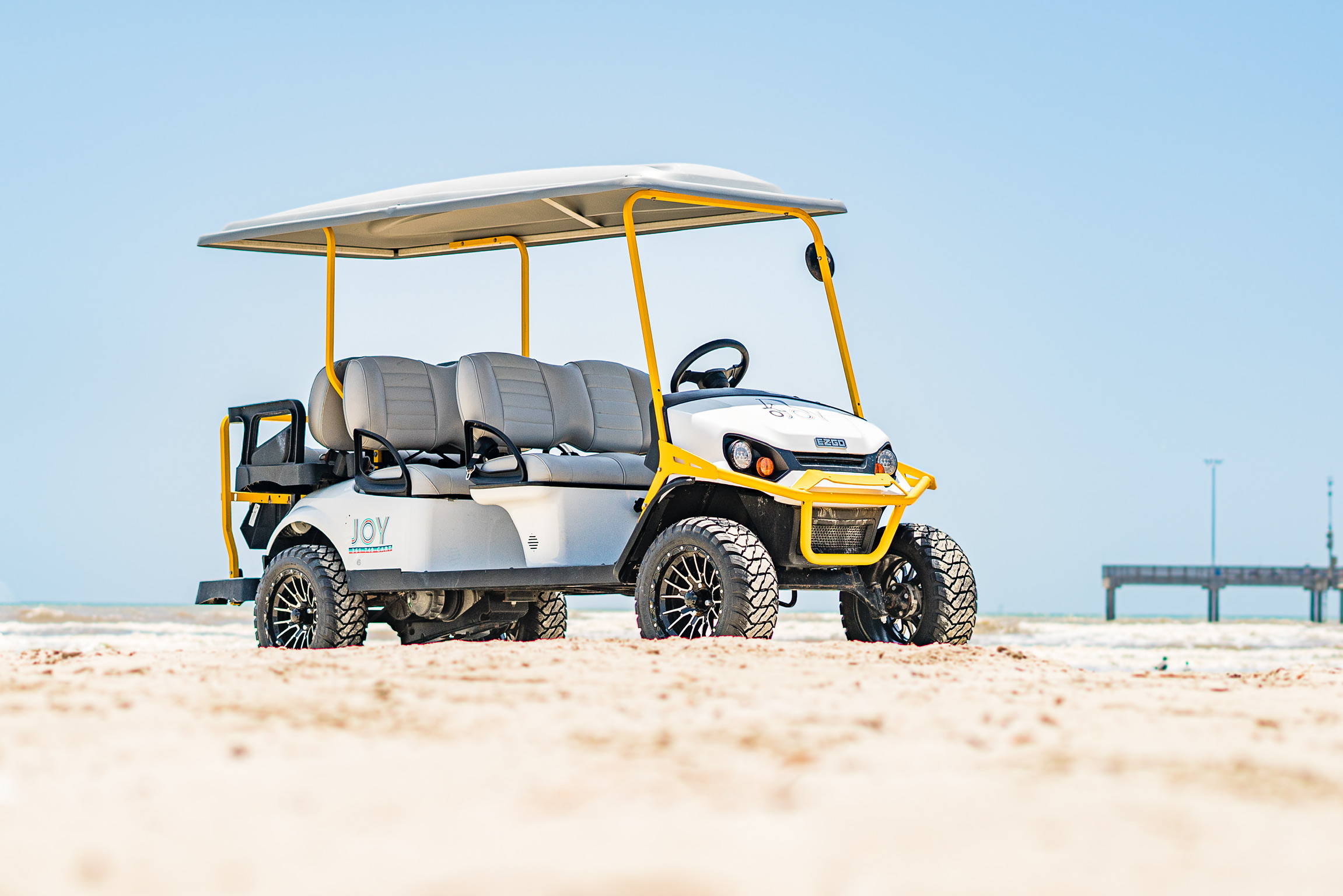 Yellow-trim Joy Cart Rentals 6-passenger E-Z-GO golf cart parked on Port Aransas beach